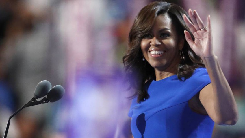 Michelle Obama com vestido azul e acenando e sorrindo na convenção democrática