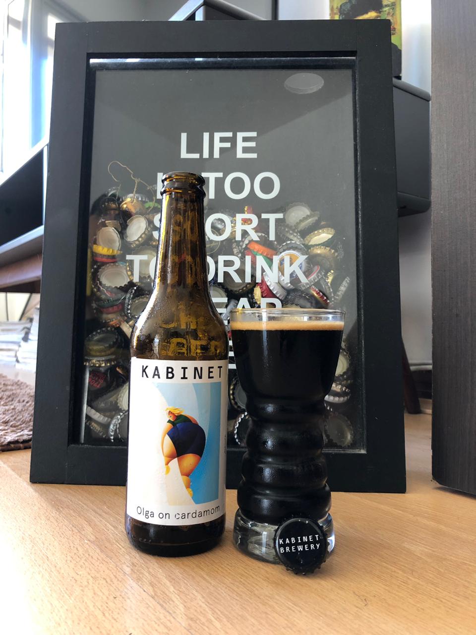 quadro de tampinhas de cerveja atrás de uma Baltic Porter da cervejaria Kabinet e copo com cerveja escura